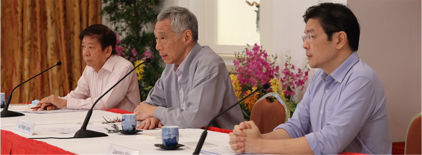 Three men at a table with microphones, teacups, and nameplates.